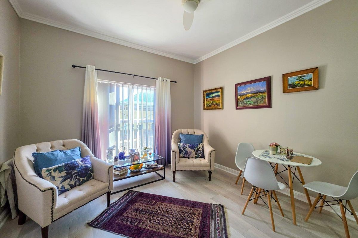 A bright and well-maintained living area featuring neutral wall tones, crown molding, a ceiling fan, and light-toned laminate flooring with access to outdoor space.