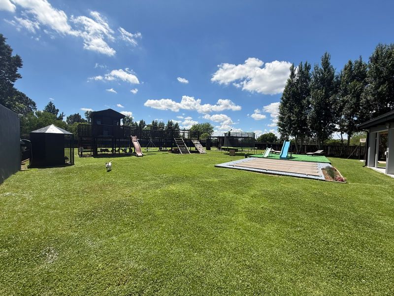 Spacious landscaped garden featuring a well-maintained lawn, perimeter fencing, and a covered swimming pool area.