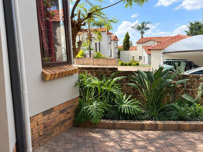 A well-maintained rear courtyard area featuring brick paving, established garden beds, and a brick boundary wall within a residential complex.