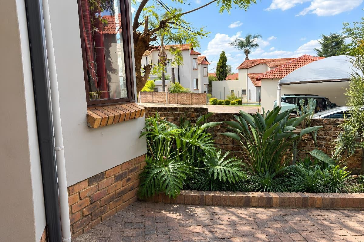 A well-maintained rear courtyard area featuring brick paving, established garden beds, and a brick boundary wall within a residential complex.