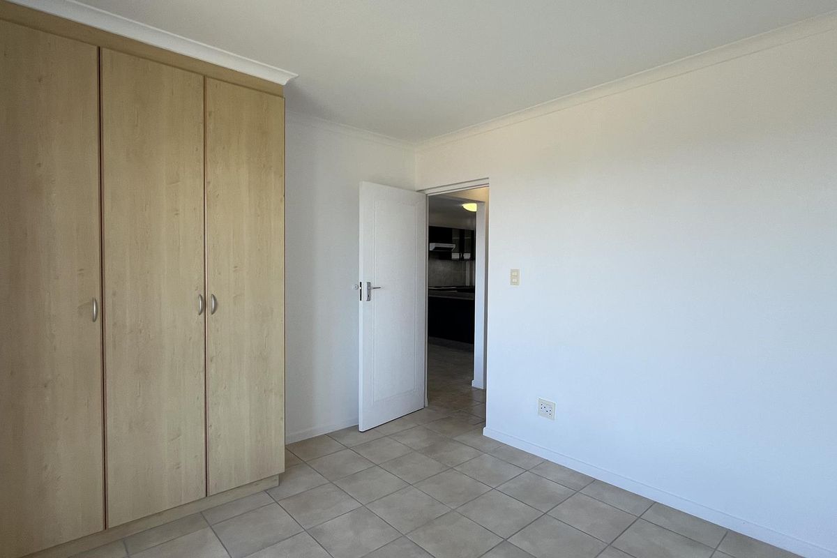 A clean, empty bedroom featuring neutral tiled flooring and a built-in wooden wardrobe, offering a blank canvas for personalization.
