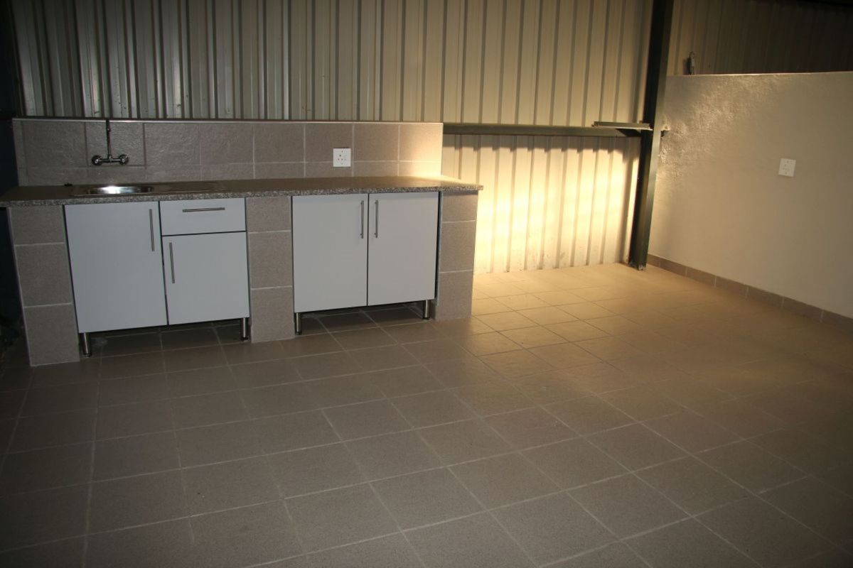 A clean, functional kitchenette area featuring tiled flooring, built-in cabinetry with a stone countertop, and a stainless steel sink against corrugated metal walls.