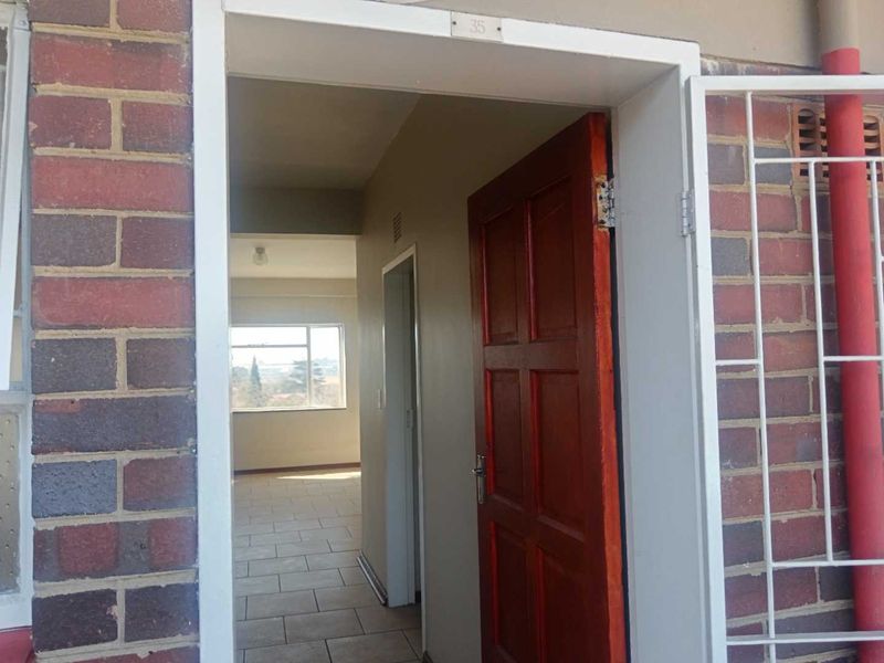 Entrance to apartment 35 featuring a brick facade, security gate, and timber door leading into a tiled interior hallway.