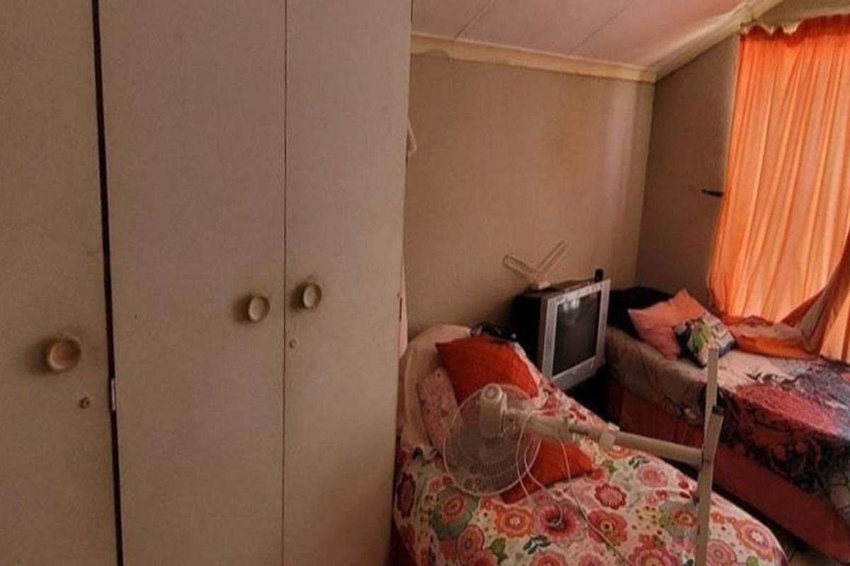 A bedroom featuring built-in cupboards and a sloped ceiling, providing functional sleeping space with potential for cosmetic updates.