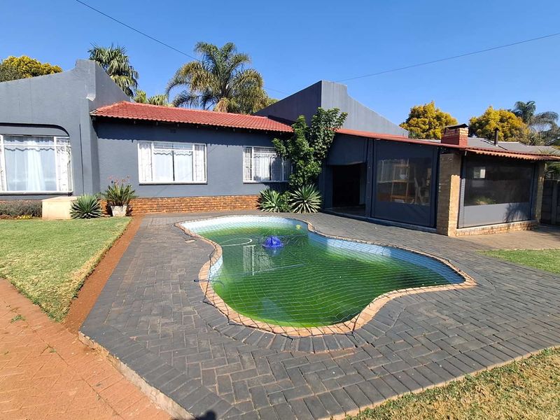 Rear exterior view featuring a swimming pool with a safety net, paved surround, and a covered patio area attached to the main house.