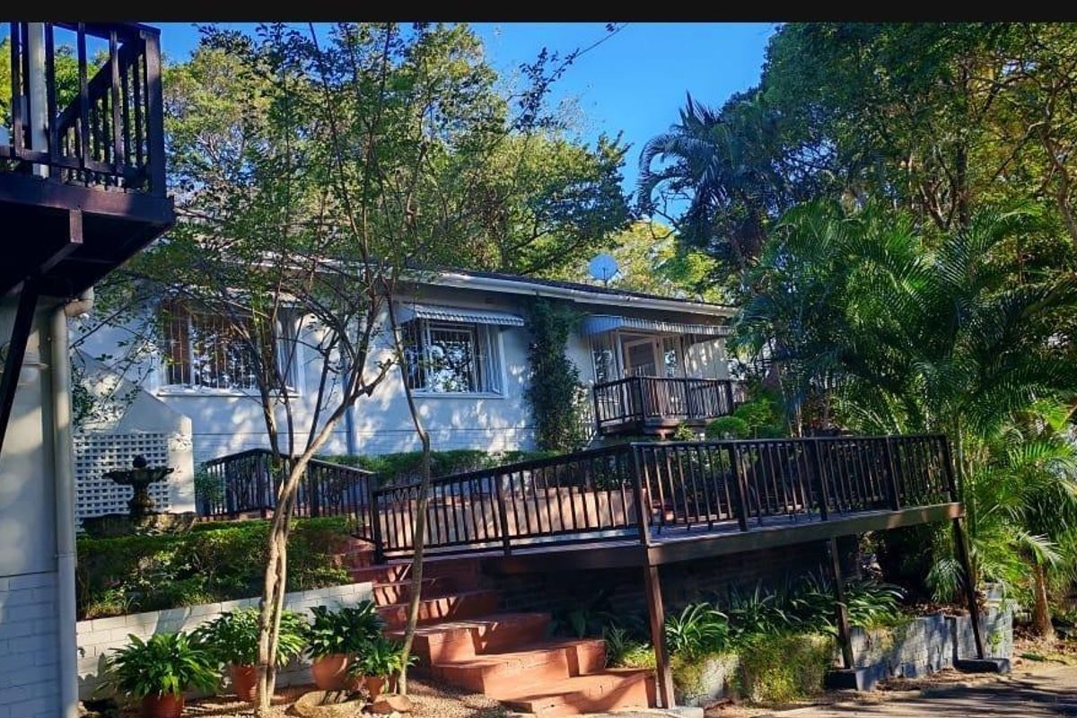 Rear exterior view of the house featuring a raised timber deck, brick staircase, and established garden surroundings with mature trees.