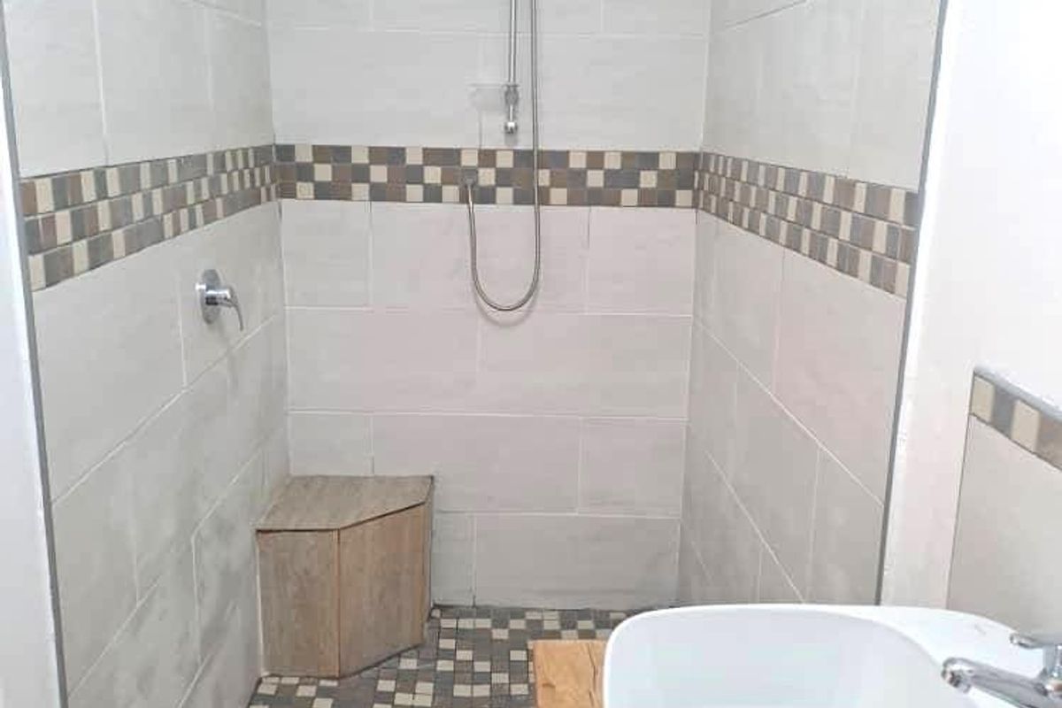 A modern bathroom featuring a walk-in shower with a built-in corner seat, tiled walls with decorative accents, and a contemporary vessel sink.