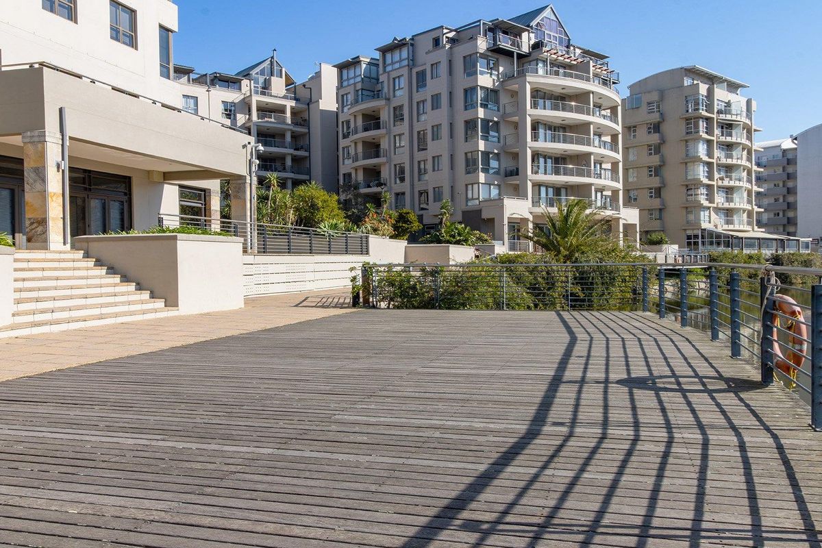 A spacious timber deck overlooking the water, featuring metal balustrades and stone stairs leading to the apartment complex exterior.