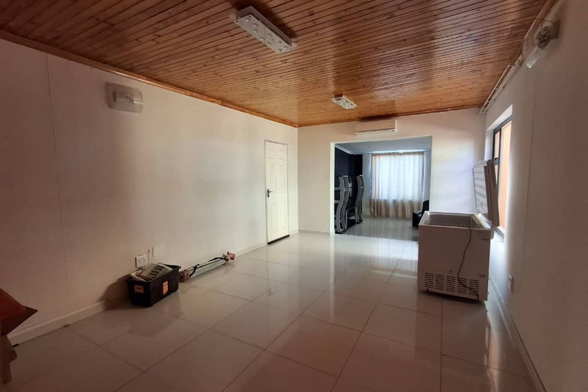 Spacious living area featuring tiled flooring, a timber-clad ceiling, and a wall-mounted air conditioning unit, leading into an adjacent room.