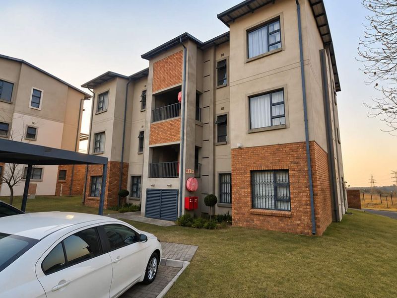 Exterior view of a multi-story apartment complex featuring brick and plaster facade, private balconies, and an adjacent covered carport area.