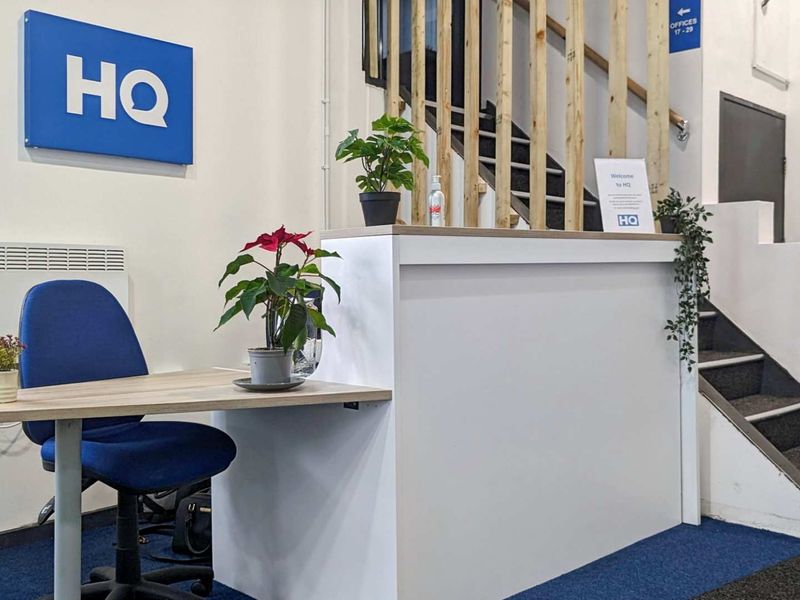 A professional office reception area featuring a built-in reception desk, carpeted flooring, and a staircase leading to upper office levels.