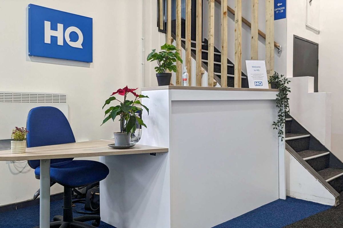A professional office reception area featuring a built-in reception desk, carpeted flooring, and a staircase leading to upper office levels.