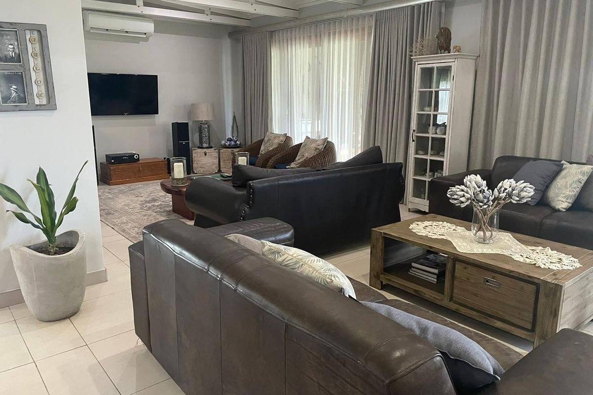 Spacious living room featuring tiled flooring, exposed beam ceiling, and wall-mounted air conditioning unit with large sliding doors leading to the exterior.