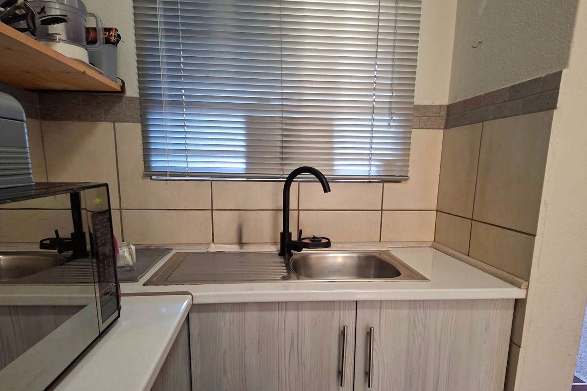 A functional kitchen area featuring a stainless steel sink, black faucet, tiled backsplash, and light wood-look cabinetry with laminate countertops.