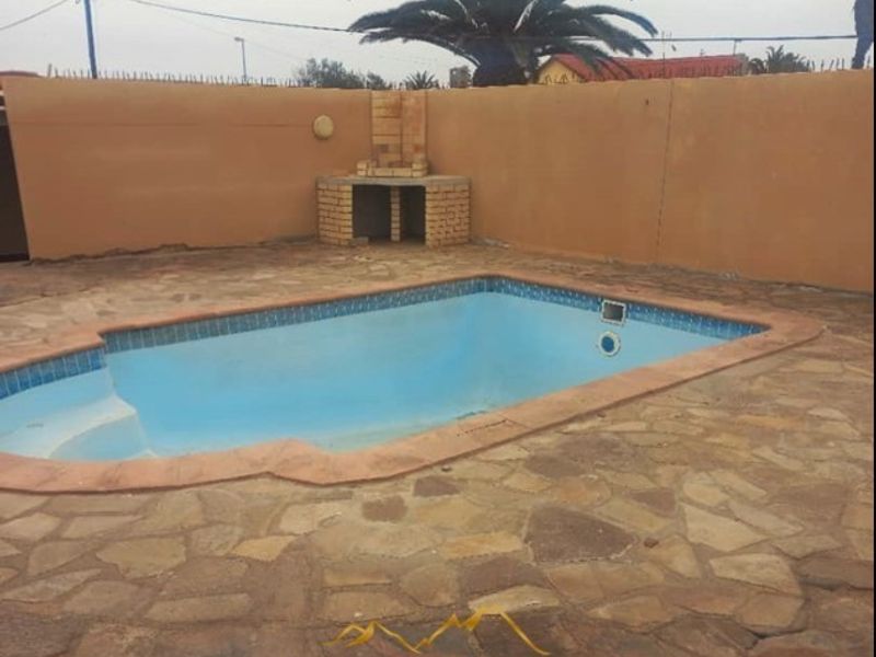 Outdoor pool area featuring a built-in brick braai, stone paving, and a perimeter boundary wall.