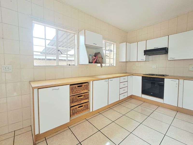 A functional kitchen featuring built-in cabinetry, laminate countertops, a built-in oven, hob, and extractor fan, finished with tiled walls and flooring.