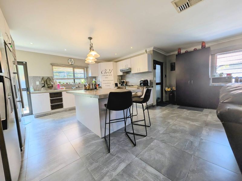 Modern kitchen featuring a central island with stone countertop, ample built-in cabinetry, recessed lighting, and large format floor tiles.