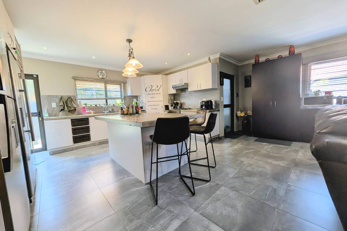 Modern kitchen featuring a central island with stone countertop, ample built-in cabinetry, recessed lighting, and large format floor tiles.