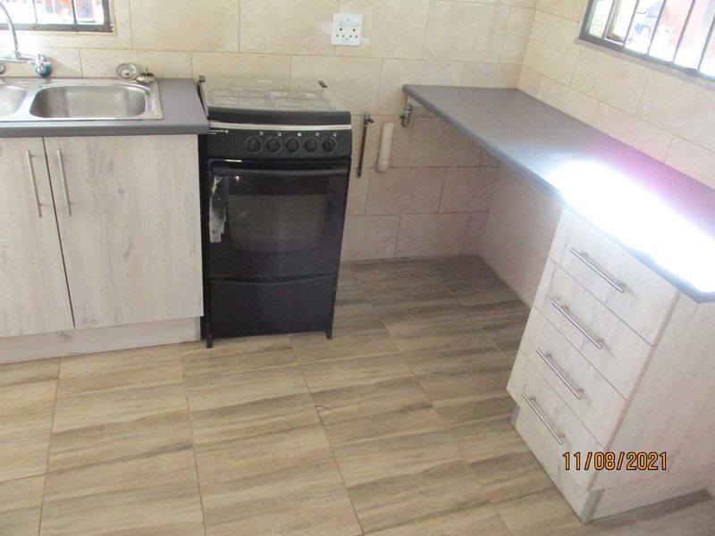 A functional kitchen featuring light wood-look cabinetry, a stainless steel sink, a freestanding gas stove, and neutral tiled finishes throughout.