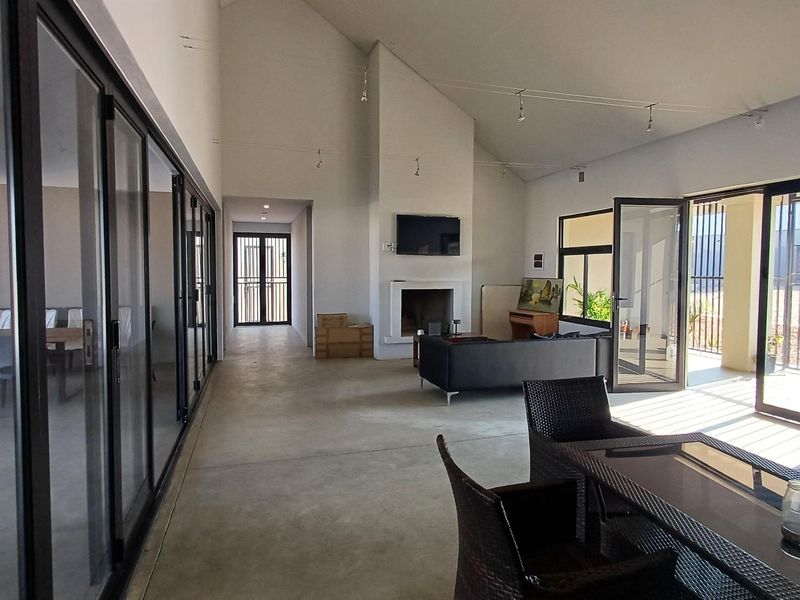 Spacious open-plan living area featuring high vaulted ceilings, polished concrete floors, a built-in fireplace, and large aluminium sliding doors leading to the outdoors.