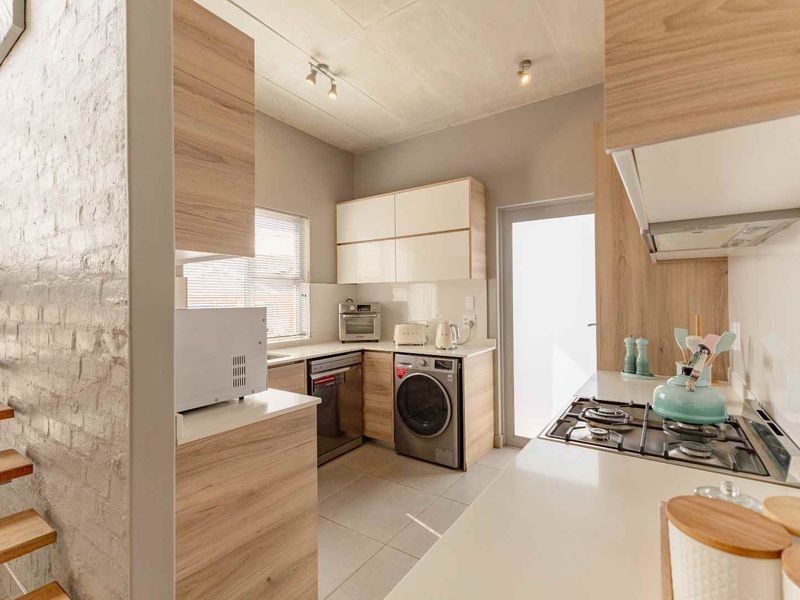 Modern kitchen featuring light wood cabinetry, gas hob, extractor fan, and tiled flooring, adjacent to an exposed brick wall and timber staircase.