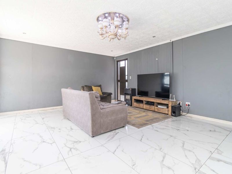 Spacious living room featuring large-format marble-look floor tiles, a decorative ceiling chandelier, and direct access to the exterior via a sliding glass door.
