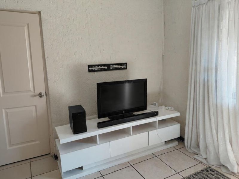 A living room area featuring tiled flooring, textured walls, and a wall-mounted television bracket.
