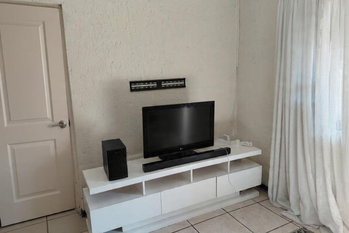 A living room area featuring tiled flooring, textured walls, and a wall-mounted television bracket.