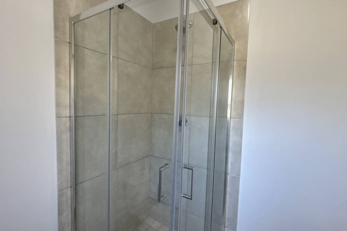 A modern bathroom shower enclosure featuring neutral-toned wall tiles and a glass door system.