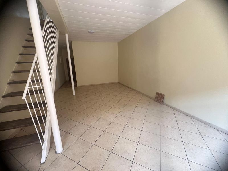 An empty, open-plan living area featuring ceramic floor tiles, a staircase with a metal balustrade, and a support column.