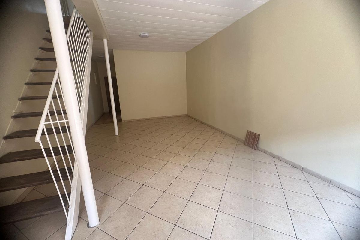 An empty, open-plan living area featuring ceramic floor tiles, a staircase with a metal balustrade, and a support column.