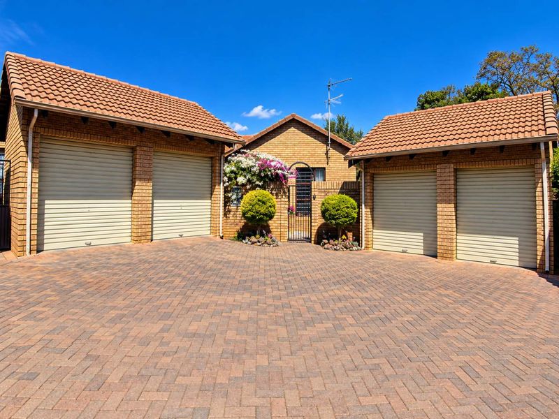 Front view of a townhouse featuring a paved driveway, four garage doors, and a secure gated entrance with brick exterior finishes.