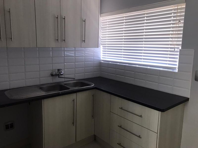 A clean and functional kitchen featuring light wood-tone cabinetry, dark laminate countertops, a double stainless steel sink, and a classic white subway tile backsplash.