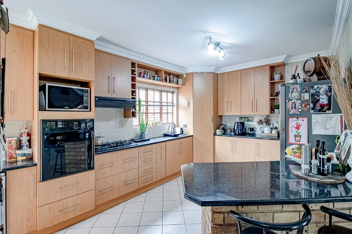 A functional kitchen featuring light wood cabinetry, dark granite countertops, a built-in oven, gas hob, and a breakfast bar island.