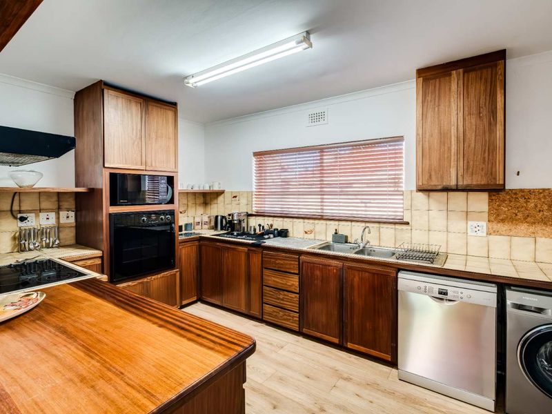A functional kitchen featuring wooden cabinetry, built-in appliances, tiled splashbacks, and a double bowl sink, offering a classic layout with potential for modernization.