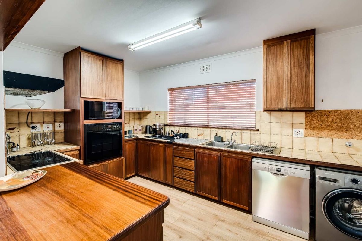A functional kitchen featuring wooden cabinetry, built-in appliances, tiled splashbacks, and a double bowl sink, offering a classic layout with potential for modernization.