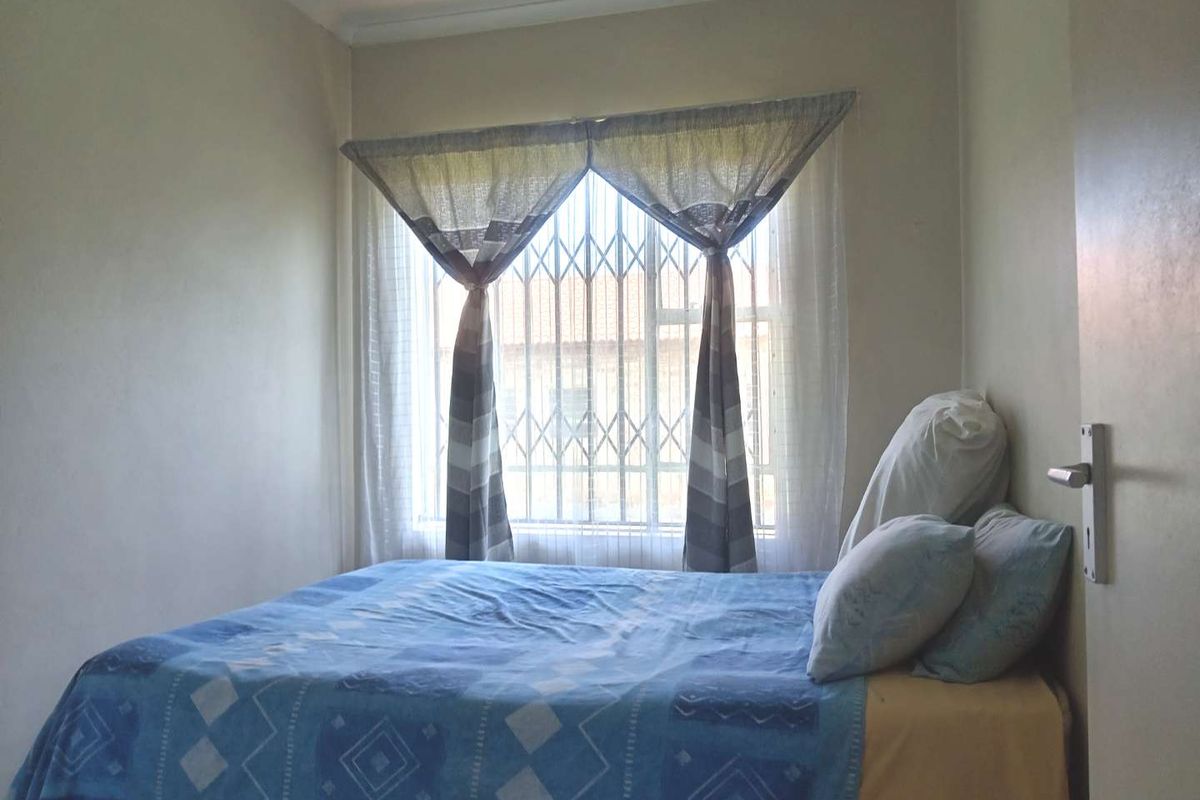 A standard bedroom featuring a window with security bars and neutral wall finishes.