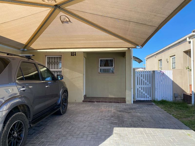 Front exterior view of the townhouse featuring a paved driveway, a protective shade sail, and a secure gated entrance.