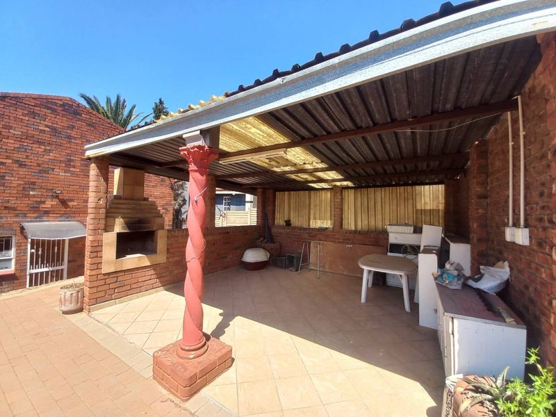 Covered outdoor patio area featuring a built-in brick braai, tiled flooring, and a decorative column, offering potential for an enhanced entertainment space.