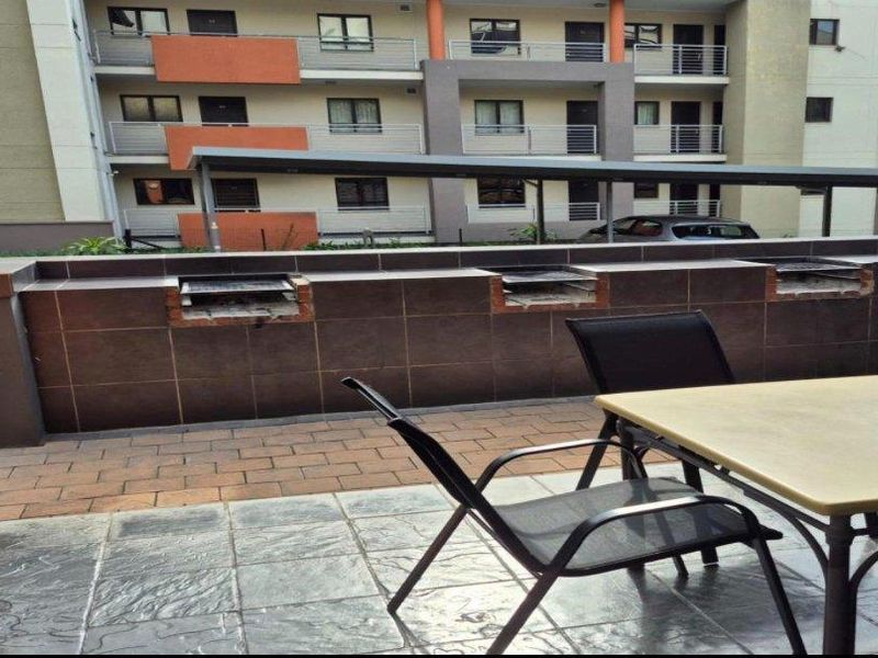 Outdoor patio area featuring a built-in braai station with tiled flooring, overlooking the apartment complex exterior.