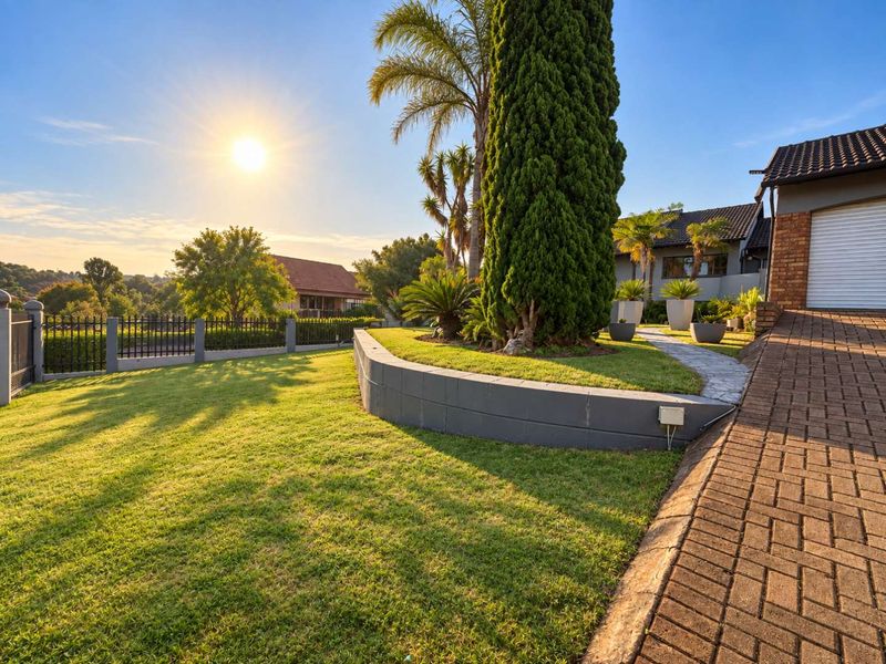 A well-maintained front exterior featuring a paved driveway, manicured lawn, landscaped garden beds with a retaining wall, and secure perimeter fencing.