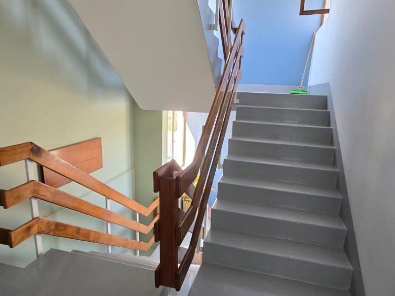 A functional apartment stairwell featuring painted concrete steps and a traditional wooden handrail system.