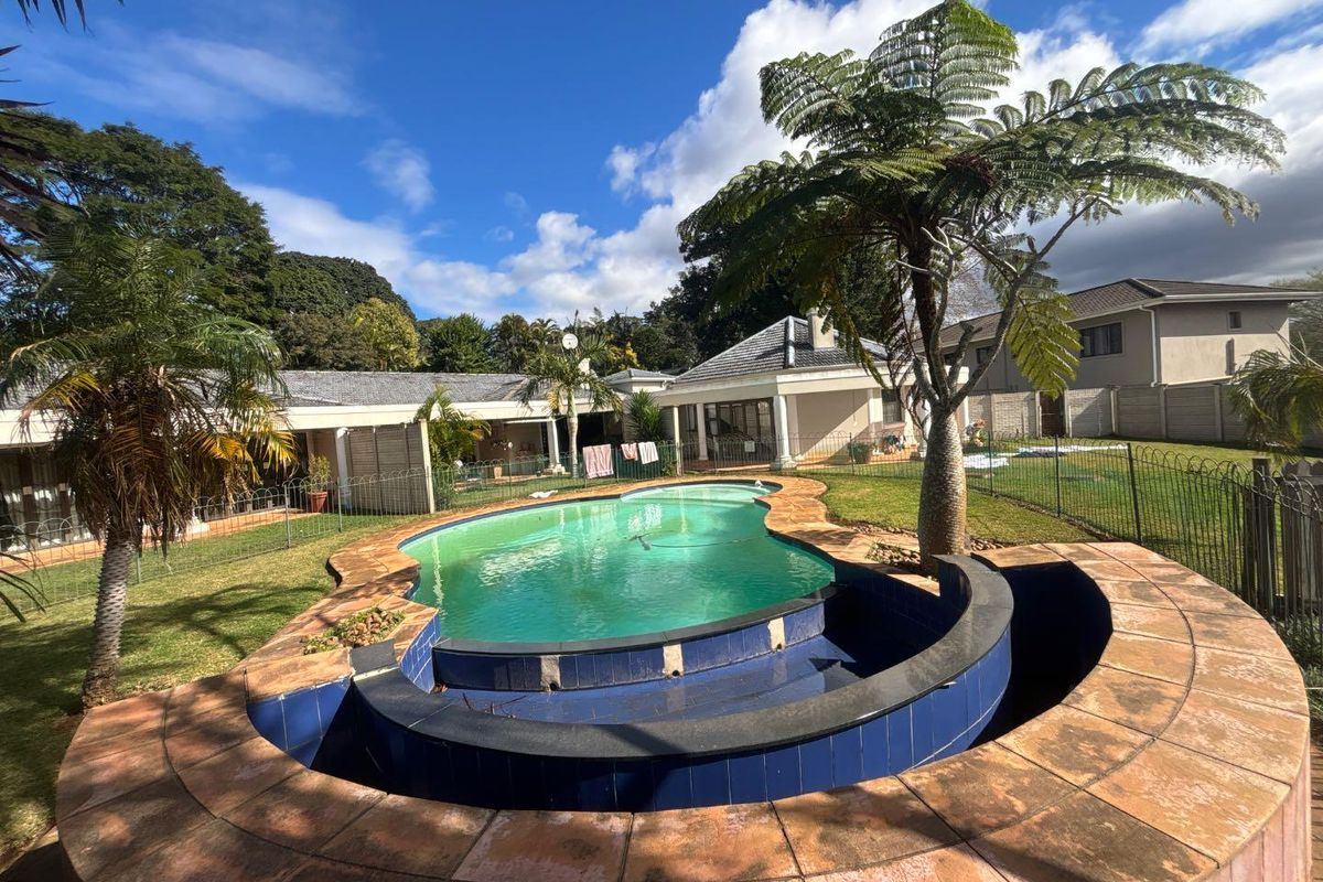 Outdoor pool area featuring a curved tiled surround, metal fencing, and established garden, requiring maintenance to the pool surface and water quality.