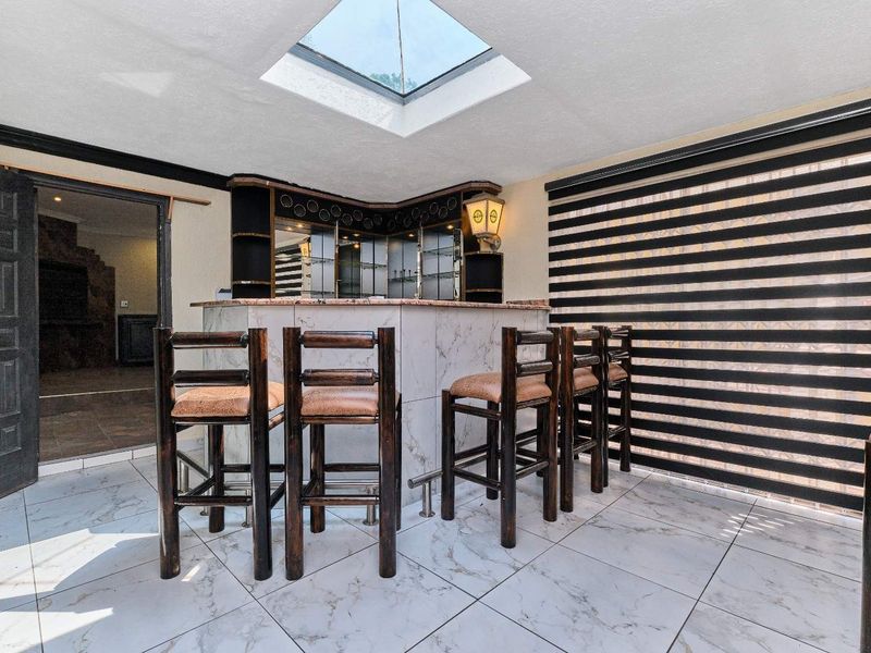 A dedicated bar area featuring a built-in counter, mirrored shelving, marble-look floor tiles, and a skylight for natural illumination.