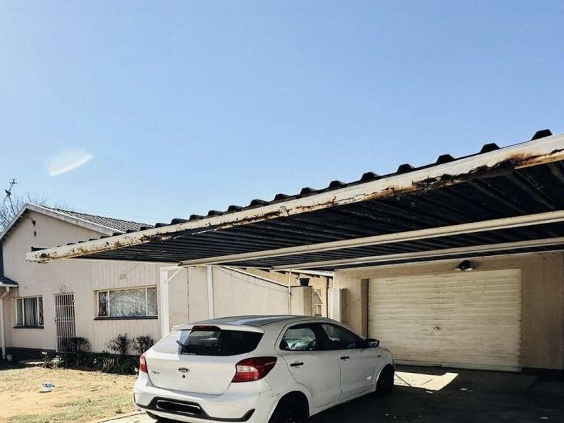 Front exterior view of the property featuring a large carport, attached garage, and tiled roof structure.