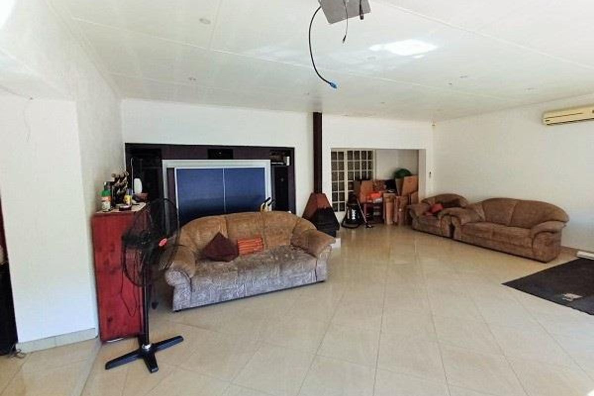 Spacious living area featuring tiled flooring, a freestanding fireplace, and wall-mounted air conditioning, requiring minor electrical repairs to the ceiling fixtures.