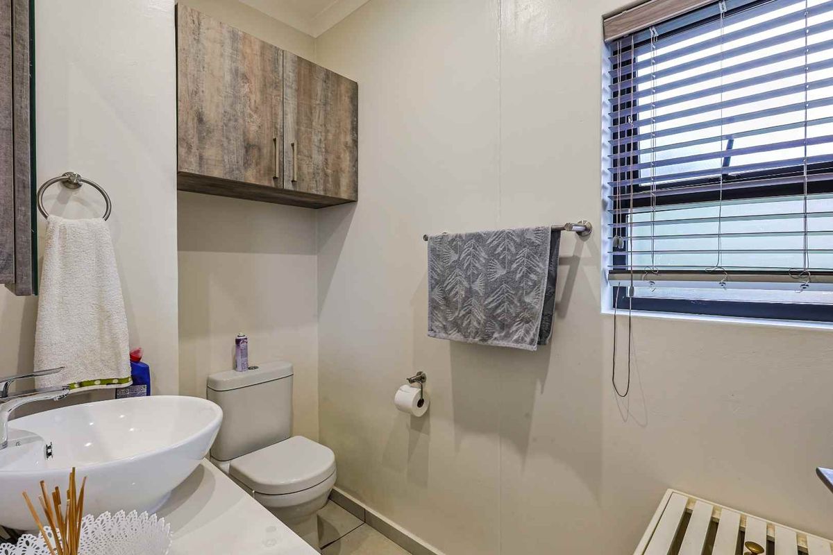 A compact bathroom featuring a modern vessel sink, wall-mounted cabinetry, a standard toilet, and a window with fitted blinds.