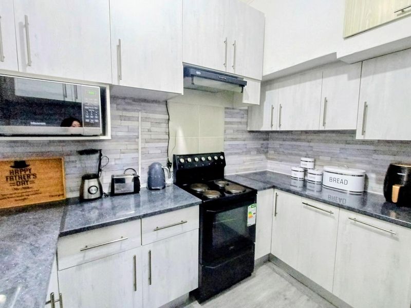 A functional kitchen featuring light-toned cabinetry, dark laminate countertops, a tiled backsplash, and a built-in microwave with a freestanding stove.