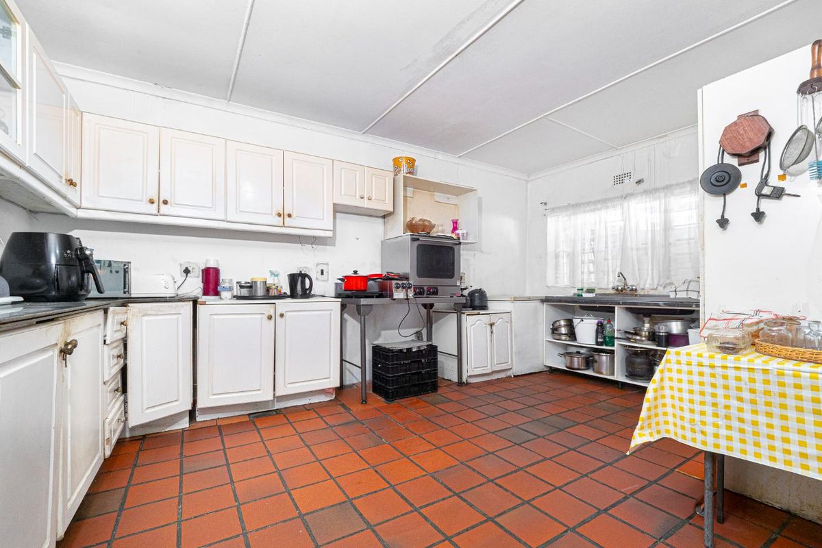A dated kitchen featuring white cabinetry, terracotta tile flooring, and a functional sink area, offering significant potential for modernization and renovation.