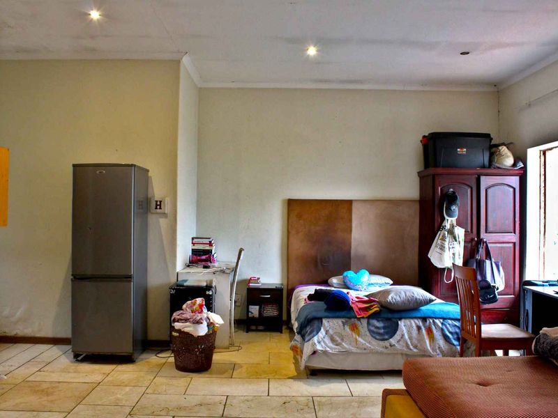 A bedroom featuring tiled flooring and recessed downlighting, currently showing signs of wear on the ceiling and floor surfaces.